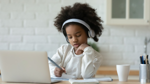 Girl with headphones works on Chromebook at kitchen table
